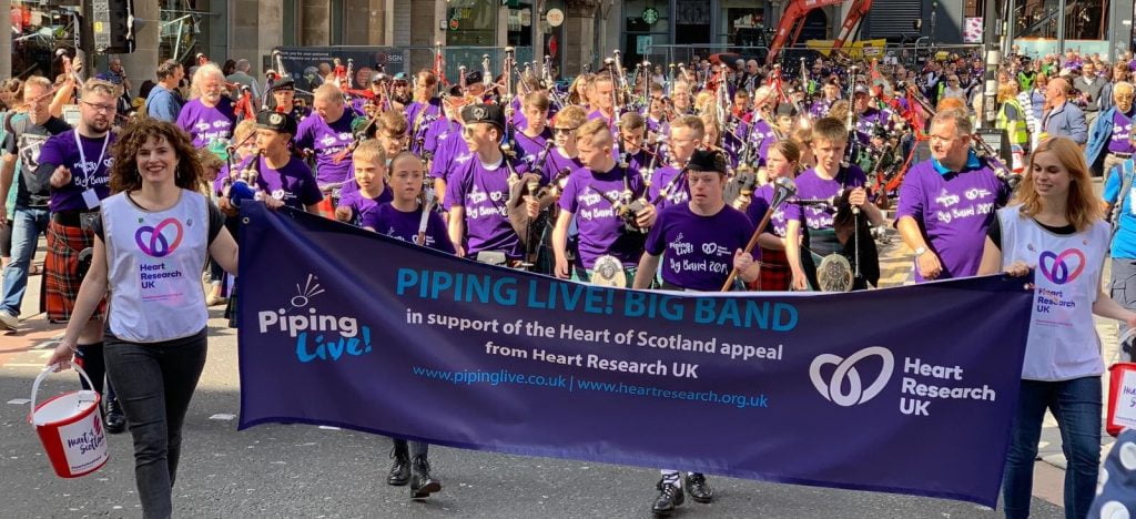 Heart Research UK staff holding up Piping Live banner leading the parade of bagpipers.