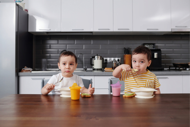 Influencing childrens eating 2 Two toddlers eating food at a breakfast bar