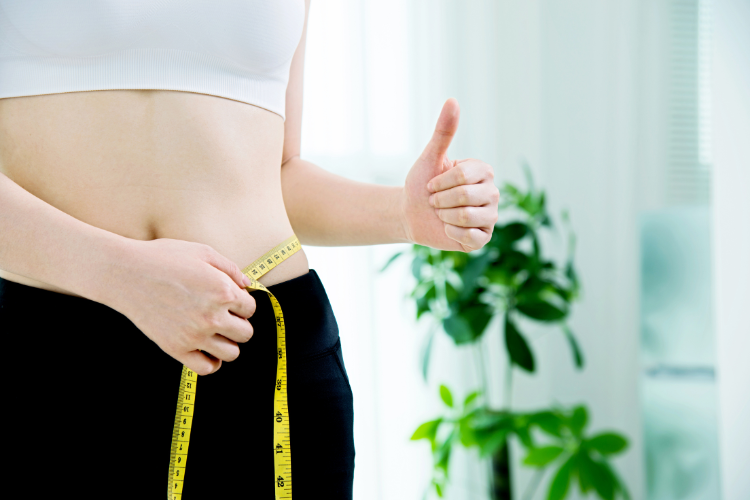 hand holding measuring tape around waist and other hand giving thumbs up