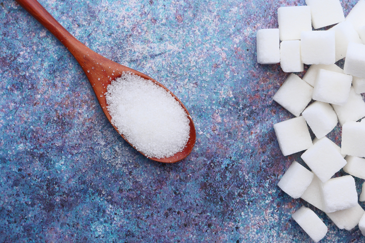 white sugar on a wooden spoon with sugar cubes in the background