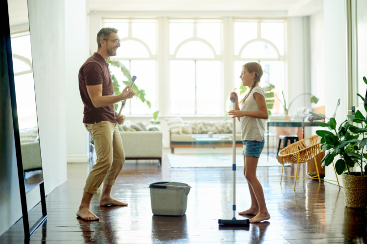 middle aged man and young girl holding floor mops looking happy