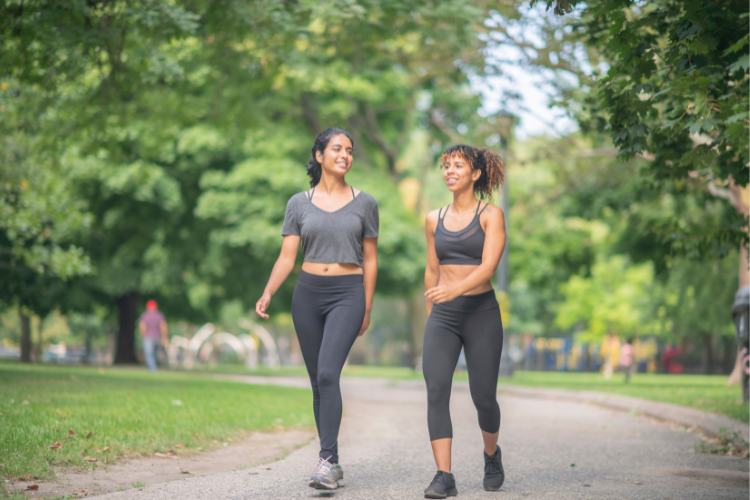 02 two female friends dressed in athleisure walking and chatting in a park walking with friends can encourage you to walk more