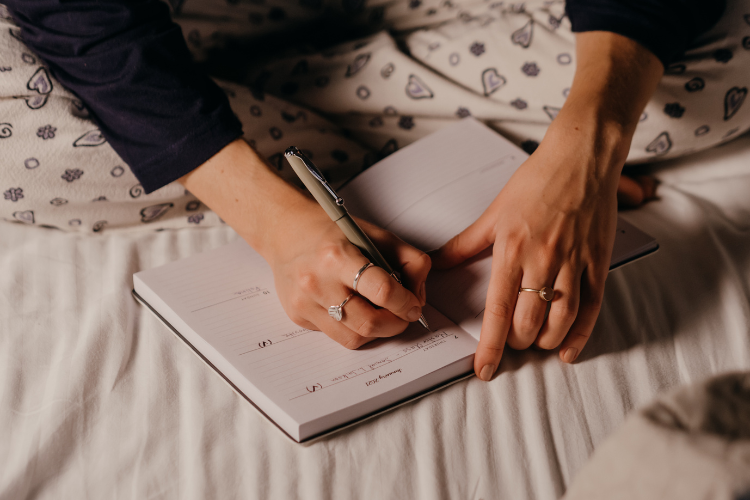 03 a woman's hand writing inside of a journal while sat on a bed