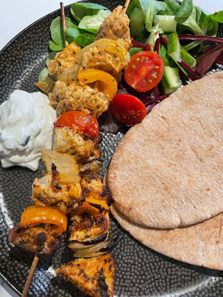 a plate with two turkey kebabs, a pitta bread, a portion of salad and sauce