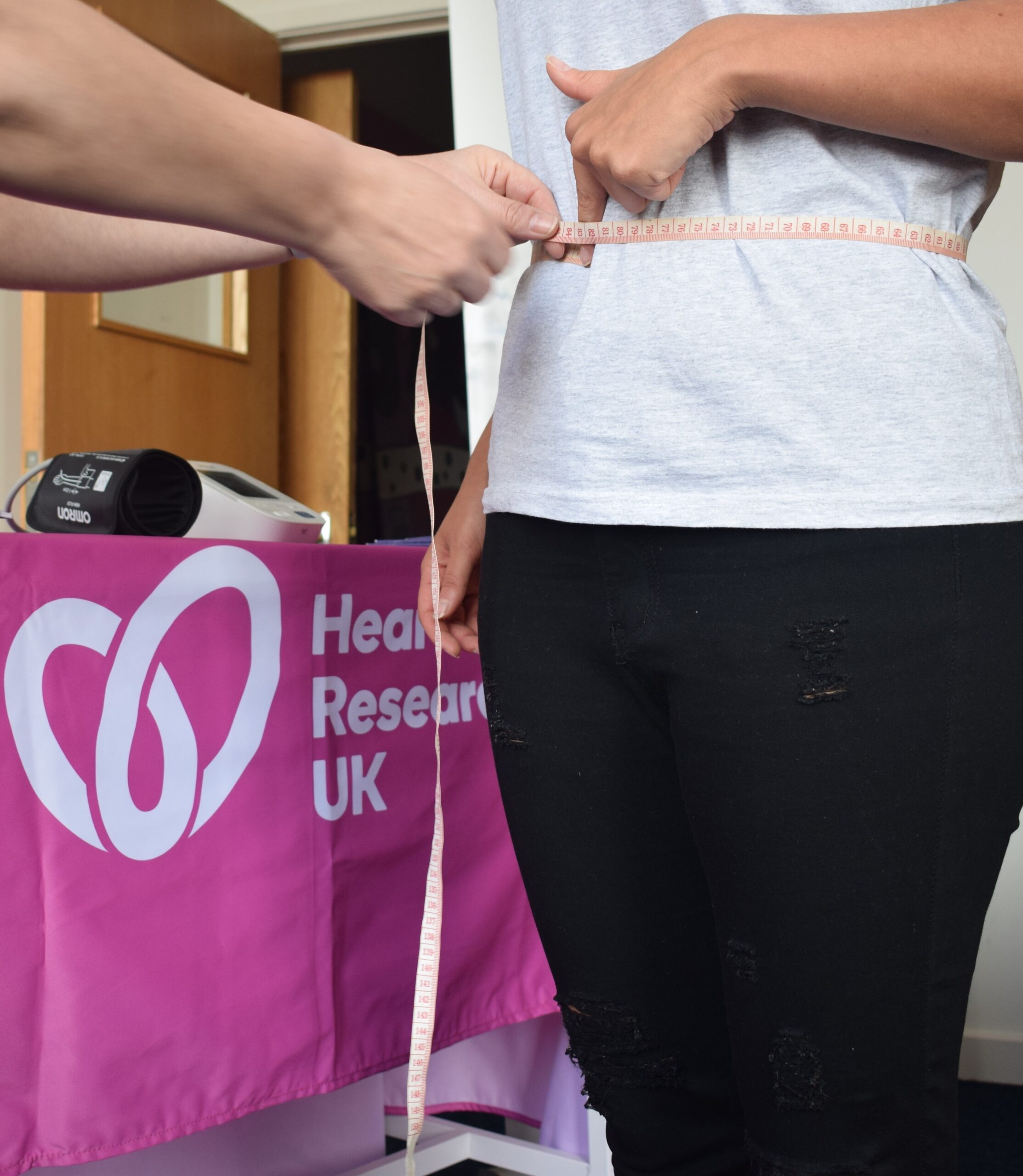 CC Aug 23 - cropped standing waist measurement, with pink tablecloth in the background with white Heart Research UK heart logo.