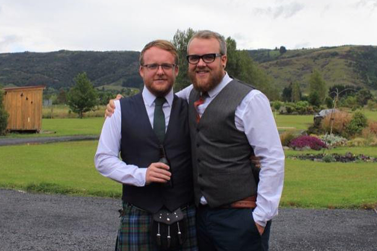Ali_and_Brother_MainLanddingPage_Image Two men standing outside. One has his arm around the other's shoulders. They are both wearing kilts