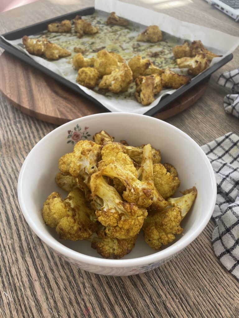 A bowl and baking tray with roasted curried cauliflower in
